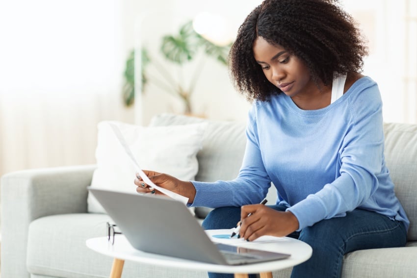 Woman Signing Papers Working On Laptop At Home C2U3VJE